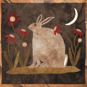 May include: A brown rabbit sits on a green patch of ground with red flowers and green leaves. A crescent moon is in the upper right corner of the image.