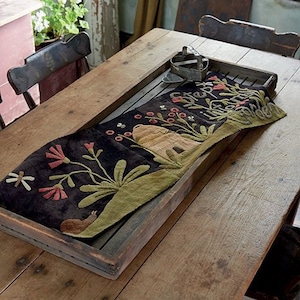 May include: A rustic wooden table with a dark brown runner featuring a floral design with a beehive, flowers, and a snail. The runner is made of fabric and has a hand-stitched look.