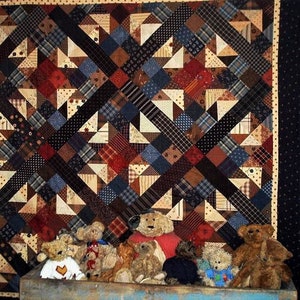 Può includere: Una trapunta patchwork con un motivo geometrico in tonalità di marrone, blu, rosso e bianco. La trapunta è esposta su una parete con una cornice in legno ed è decorata con diversi orsacchiotti.