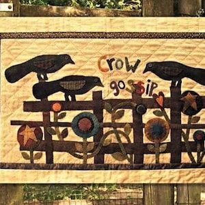 Op de afbeelding: Een bruine en beige gequilte wandhanger met een bruin hek en drie zwarte kraaien. De kraaien zitten op het hek en de tekst "Crow Gossip" is in bruine letters boven het hek geschreven.
