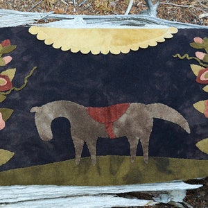 May include: A brown horse with a red saddle stands in a field of green flowers under a yellow moon. The horse is silhouetted against a dark blue background.