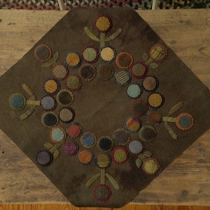 Peut inclure: Un chemin de table en feutre brun avec un motif circulaire de cercles et de fleurs en feutre de couleurs vives. Les cercles sont disposés en anneau autour d'un cercle central, et les fleurs sont placées aux coins du chemin de table.