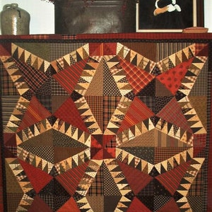 Puede incluir: Un edredón hecho a mano con un diseño de estrella, con varias telas en tonos de rojo, marrón y beige. El edredón se exhibe en un estante con un retrato enmarcado, un cubo de metal y una jarra de cerámica.