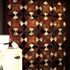 Può includere: Una grande trapunta fatta a mano con un motivo geometrico a stella. La trapunta presenta un design patchwork nei toni del marrone, nero, crema e rosso. La trapunta è probabilmente realizzata in cotone o in un tessuto simile.