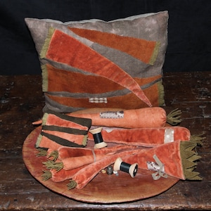 May include: A collection of handmade carrot-shaped pincushions in shades of orange and brown, arranged on a wooden tray with spools of thread and other sewing supplies. The pincushions are made from fabric and have a rustic, vintage aesthetic.