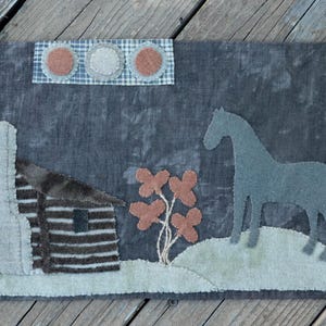 May include: A gray and white wool rug with a farmhouse theme. The rug features a cabin, a horse, a bird, and flowers. The rug is perfect for adding a touch of country charm to any room.