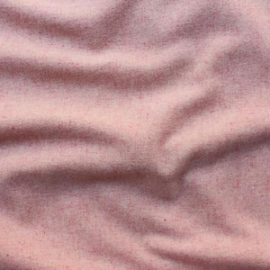 May include: A soft, light pink fabric with a subtle heathered texture and visible flecks of darker pink throughout. The material is draped in gentle, flowing folds, creating a series of soft shadows and highlights across the surface of the textile.