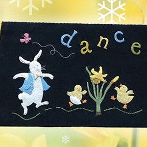 May include: A black felt wall hanging with yellow borders. The center features a white rabbit dancing with the word "dance" in colorful letters. The border text reads "and then my heart will pleasure fill and dances with the daffodils."