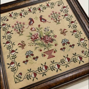 May include: A framed cross-stitch embroidery depicting a floral bouquet in a pot, surrounded by birds, trees, and a decorative border. The embroidery is worked in shades of red, green, and white.