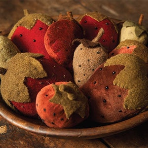 May include: A wooden bowl filled with handmade strawberry ornaments. The strawberries are various shades of red, brown, and tan, with green and brown leafy tops. Some have black seed details. The bowl sits on a wooden surface.