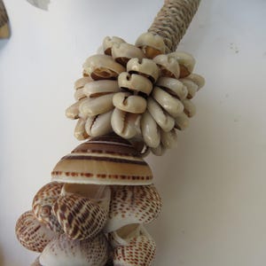 K&ouml;nnte beinhalten: Eine braune und wei&szlig;e Muschelkette mit einem gro&szlig;en B&uuml;ndel wei&szlig;er Kaurischnecken in der Mitte.