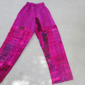 May include: Pink patchwork pants with a colorful geometric pattern. The pants have an elastic waistband and a relaxed fit.
