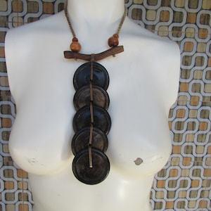 May include: A wooden necklace with a brown cord and five round wooden beads. The beads are strung on the cord and hang from a wooden branch. The necklace is displayed on a white mannequin.