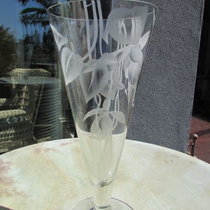 Puede incluir: Un jarr&oacute;n de cristal transparente con la parte superior acampanada y una base redonda. El jarr&oacute;n est&aacute; grabado con un dise&ntilde;o floral de hojas y flores. El jarr&oacute;n est&aacute; sobre una mesa redonda.