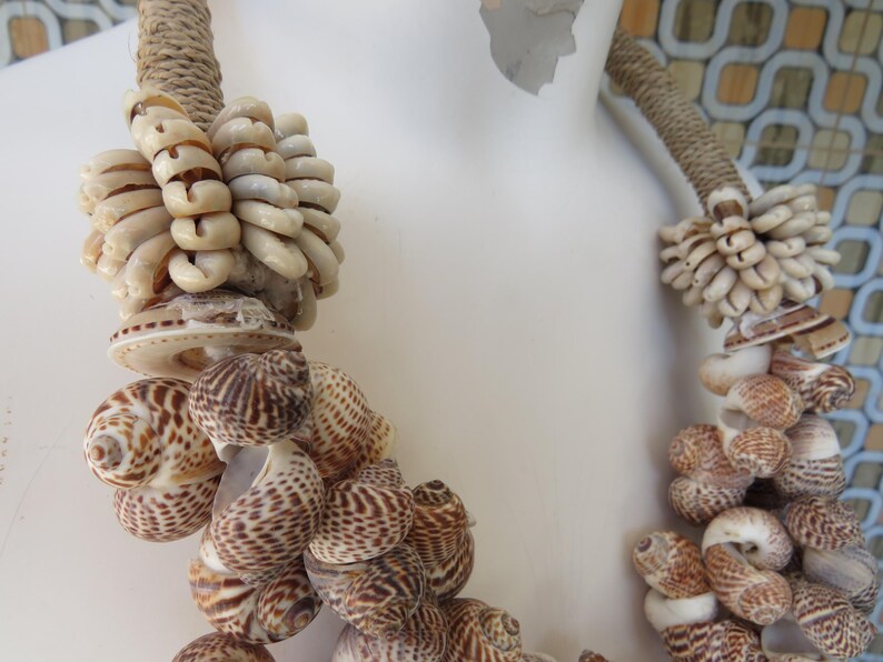K&ouml;nnte beinhalten: Eine braune und wei&szlig;e Muschelkette mit verschiedenen Muscheln in unterschiedlichen Gr&ouml;&szlig;en. Die Kette ist aus nat&uuml;rlichen Materialien gefertigt und hat einen rustikalen Look.
