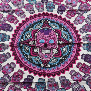 May include: A white tapestry with a pink, blue, and black mandala design featuring a large sugar skull in the center. The mandala is surrounded by a ring of smaller sugar skulls.