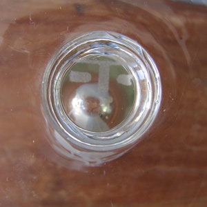 Puede incluir: Un objeto de vidrio transparente con un dise&ntilde;o circular, posiblemente un vaso o un elemento decorativo. El vidrio tiene una superficie reflectante y el fondo es de color marr&oacute;n c&aacute;lido. El objeto est&aacute; centrado en el marco.