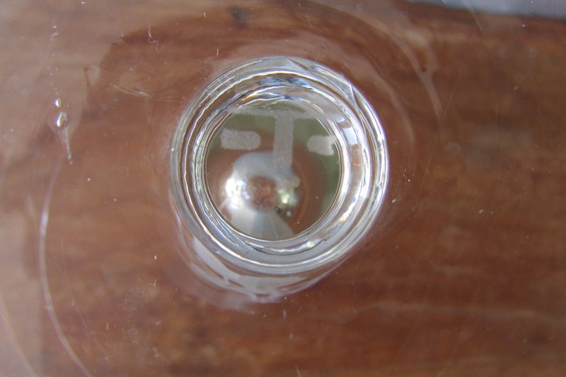 Puede incluir: Un objeto de vidrio transparente con un dise&ntilde;o circular, posiblemente un vaso o un elemento decorativo. El vidrio tiene una superficie reflectante y el fondo es de color marr&oacute;n c&aacute;lido. El objeto est&aacute; centrado en el marco.