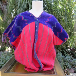 May include: A red and purple striped blouse with a geometric pattern on the shoulders. The blouse is made of a soft, woven fabric and has a V-neck.