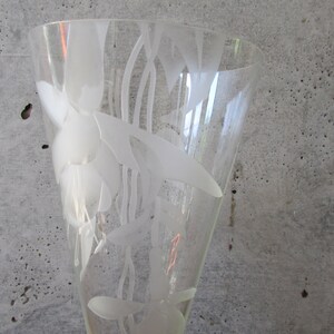 Puede incluir: Un jarr&oacute;n de cristal transparente con la parte superior acampanada, con un dise&ntilde;o floral grabado. El jarr&oacute;n tiene una forma alta y esbelta y est&aacute; decorado con patrones blancos estilizados de flores y hojas. El jarr&oacute;n se utiliza probablemente con fines decorativos.