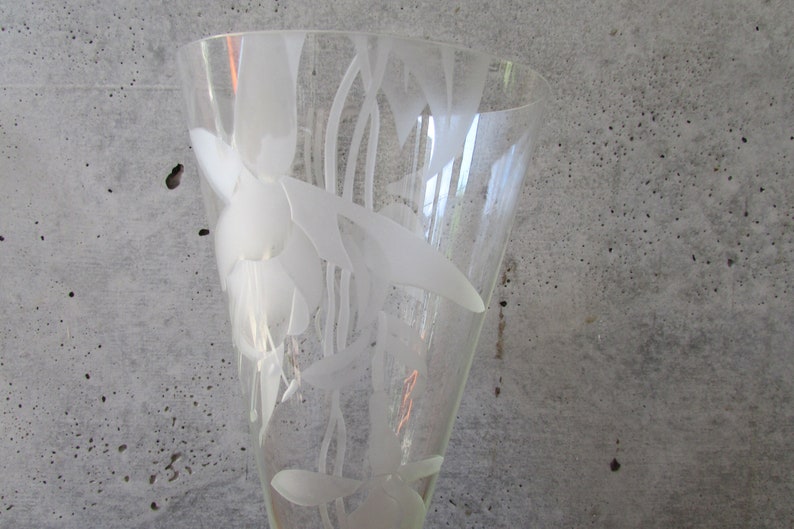 Puede incluir: Un jarr&oacute;n de cristal transparente con la parte superior acampanada, con un dise&ntilde;o floral grabado. El jarr&oacute;n tiene una forma alta y esbelta y est&aacute; decorado con patrones blancos estilizados de flores y hojas. El jarr&oacute;n se utiliza probablemente con fines decorativos.