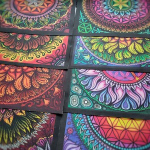 May include: A collection of rectangular fabric patches with vibrant, colorful mandala designs. Each patch features a unique, intricate pattern in shades of red, orange, yellow, green, blue, and purple, with black borders. The designs are detailed and symmetrical.