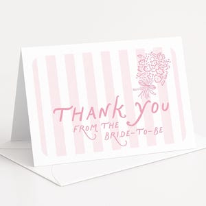 May include: A folded white card with a pink striped background and the words "Thank You From The Bride-To-Be" in pink script. A pink floral bouquet is in the upper right corner. The card is on top of a white envelope.