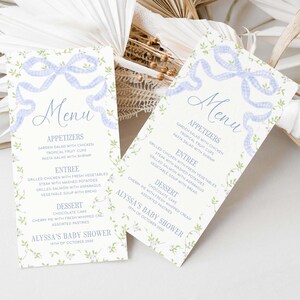May include: Two menu cards for a baby shower. The cards have a light blue gingham ribbon design at the top and floral accents. The menu includes appetizers, entrees, and desserts. The baby shower is for Alyssa, and the date is October 19th, 2030.