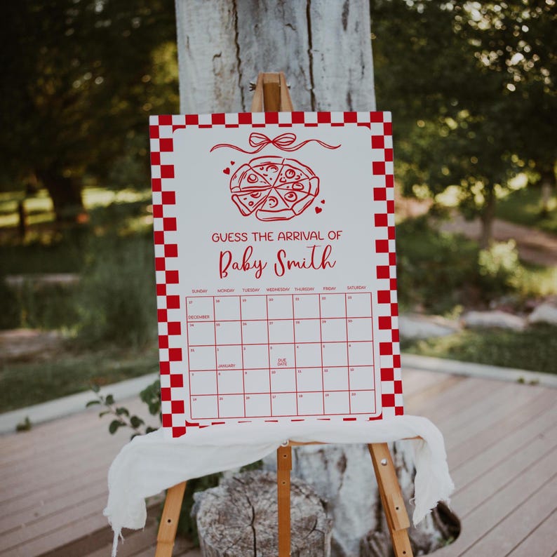 May include: A white sign with a red checkered border and a pizza graphic at the top. The text "GUESS THE ARRIVAL OF Baby Smith" is displayed above a calendar grid. The sign is mounted on a wooden easel.
