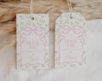 Könnte beinhalten: Zwei weiße Geschenkanhänger mit rosa Schleifen und floralen Designs. Die Anhänger tragen die Aufschrift "THANK YOU" und "for celebrating with us!" mit dem Namen "Alyssa" darunter. Jeder Anhänger hat eine Schnur zum Aufhängen.