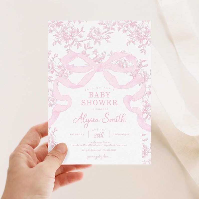 May include: A baby shower invitation with a pink floral and ribbon design. The invitation includes the text "BABY SHOWER in honor of Alyssa Smith" and event details. The invitation is held in a hand.