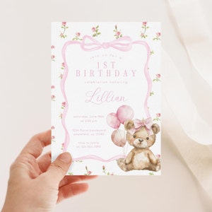 May include: Pink and white first birthday party invitation with a watercolor illustration of a teddy bear holding pink balloons. The invitation includes the text "Join us for a 1st Birthday celebration honoring Lillian".