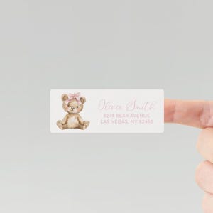 May include: A white rectangular return address label with a watercolor illustration of a brown teddy bear wearing a pink bow. The text "Olivia Smith", "8274 Bear Avenue", and "Las Vegas, NV 82458" is printed in pink.