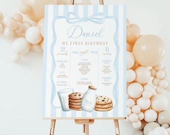 May include: A blue and white striped first birthday poster featuring a watercolour illustration of a glass of milk and cookies. The poster includes the child's name, Daniel, and details about their first year, including their weight, height, favourite toys, and first words.