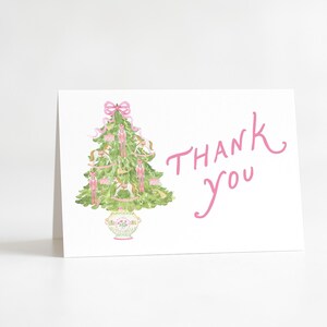 May include: A white greeting card with a watercolor illustration of a Christmas tree decorated with pink bows and nutcrackers. The words "Thank you" are written in pink script.