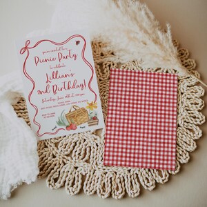 May include: A red and white gingham patterned card with a white card on top. The white card has a red border and red text that says "You're invited to a Picnic Party to celebrate Lillian's 2nd Birthday!"  The text also includes the date, time, and location of the party.