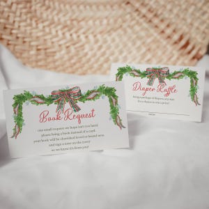 May include: Two white cards with watercolour illustrations. One reads "Book Request" with text below. The other says "Diaper Raffle". Both cards feature a green garland with red and green plaid bows, ideal for a baby shower or festive occasion.