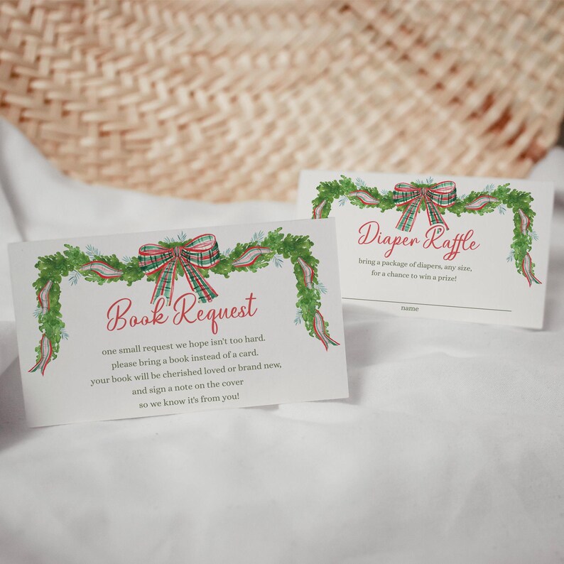 May include: Two white cards with watercolour illustrations. One reads "Book Request" with text below. The other says "Diaper Raffle". Both cards feature a green garland with red and green plaid bows, ideal for a baby shower or festive occasion.