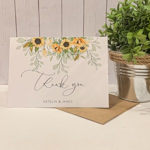 May include: A white thank you card with a watercolor design of sunflowers and greenery. The text "Thank you" is written in cursive script. The names "KATELIN & JAMES" are printed below the text.