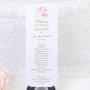 May include: A wedding program with a floral design at the top. The program includes the names Jessica Hall and Jonathan Smith, the date July 16, 2018, and the ceremony details. The program is displayed on a black stand.