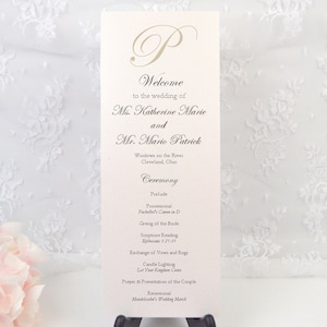 May include: A wedding ceremony program with a white background and black text. The program lists the names of the bride and groom, the ceremony location, and the order of events. The text includes "Welcome to the wedding of Ms. Katherine Marie and Mr. Mario Patrick", "Windows on the River, Cleveland, Ohio", "Ceremony", "Prelude", "Processional", "Pachelbel's Canon in D", "Giving of the Bride", "Scripture Reading", "Exchange of Vows and Rings", "Candle Lighting", "Let Your Light Shine", "Prayer & Presentation of the Couple", "Recessional", "Mendelssohn's Wedding March".