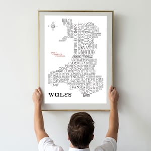 May include: A black and white word cloud in the shape of Wales. The word cloud includes the names of cities, towns, and geographical features in Wales. The word "Wales" is written in large, bold letters at the bottom of the image.
