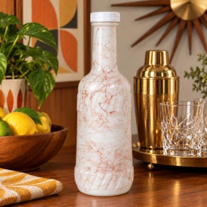 May include: A tall, cylindrical glass bottle with a white opaque finish and a delicate, thin red marbled or webbed pattern throughout the surface. The bottle features a narrow neck, a white screw-top cap, and a textured, rope-like design at the base.