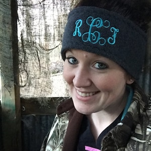 May include: A woman wearing a gray fleece headband with the monogram "R.E.J." embroidered in turquoise blue. She is wearing a camouflage jacket and a black shirt.