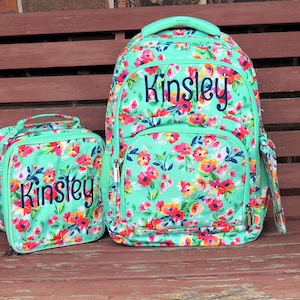 May include: A turquoise floral backpack and matching lunch bag with the name "Kinsley" embroidered on both.
