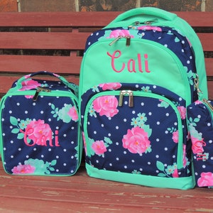 May include: A blue and green floral backpack with a matching lunch bag and pencil case. The backpack has a green top flap with the name "Cali" embroidered in pink.