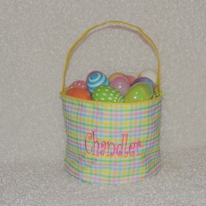May include: A pastel plaid Easter basket with a yellow handle, filled with colorful Easter eggs. The basket has the name "Chandler" embroidered on the front. The eggs are various colors and patterns.