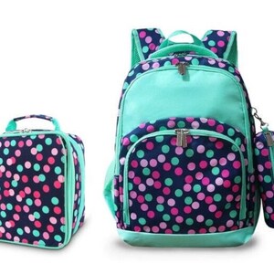 May include: A set of three school bags in a polka dot pattern. The backpack is turquoise and navy blue with pink and green polka dots. The lunch bag and pencil case are navy blue with pink and green polka dots and a turquoise trim.
