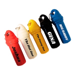 May include: Five colorful, cylindrical keychains in red, white, yellow, black, and blue. Each keychain has a silver ring and features a different name or phrase in white text: "Joshua", "The Hot One", "The Funny One", "Gina", and "Big Daddy".