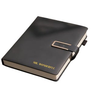 May include: Black notebook with a gold clasp and the words "MR. WONDERFUL" in gold lettering. The notebook has a strap closure and cream-colored edges. A stylish and practical item for note-taking and journaling.
